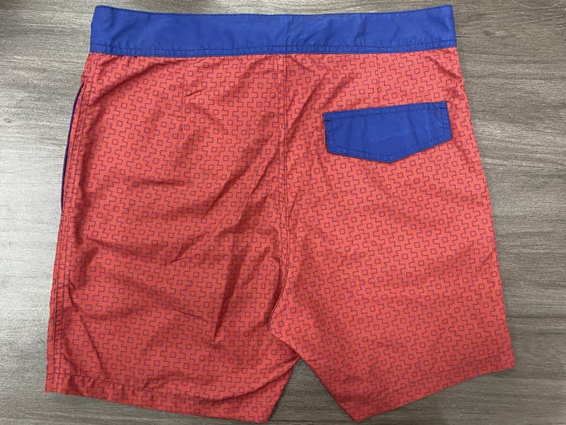 Back view of coral micro-geometric board shorts with blue pocket