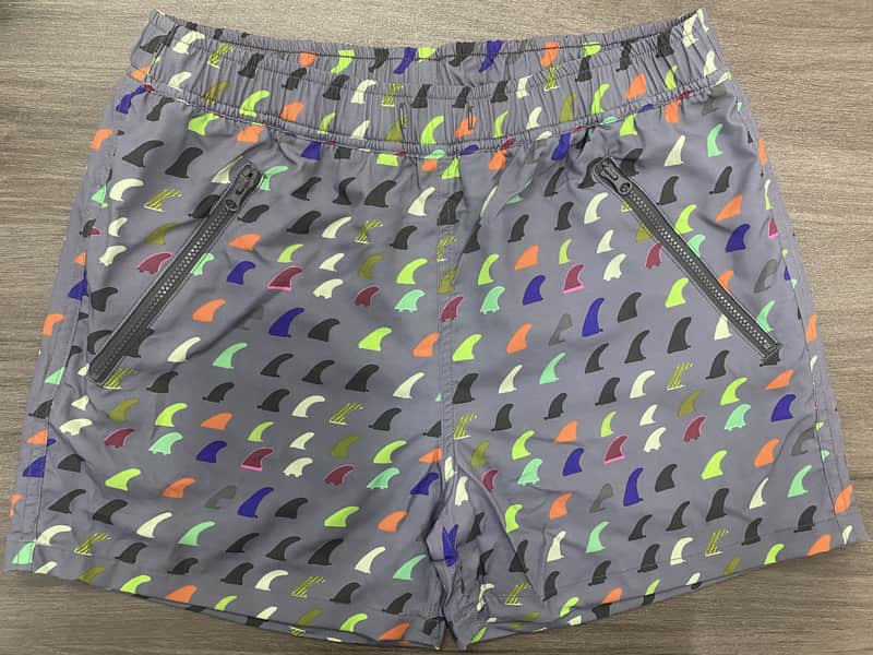 Front view of self-owned gray swim shorts with multicolor fin print and angled zipper pockets