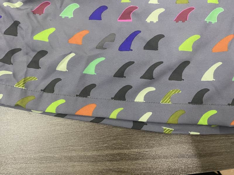 Hem and repeat-scale detail on gray multicolor fin print swim shorts