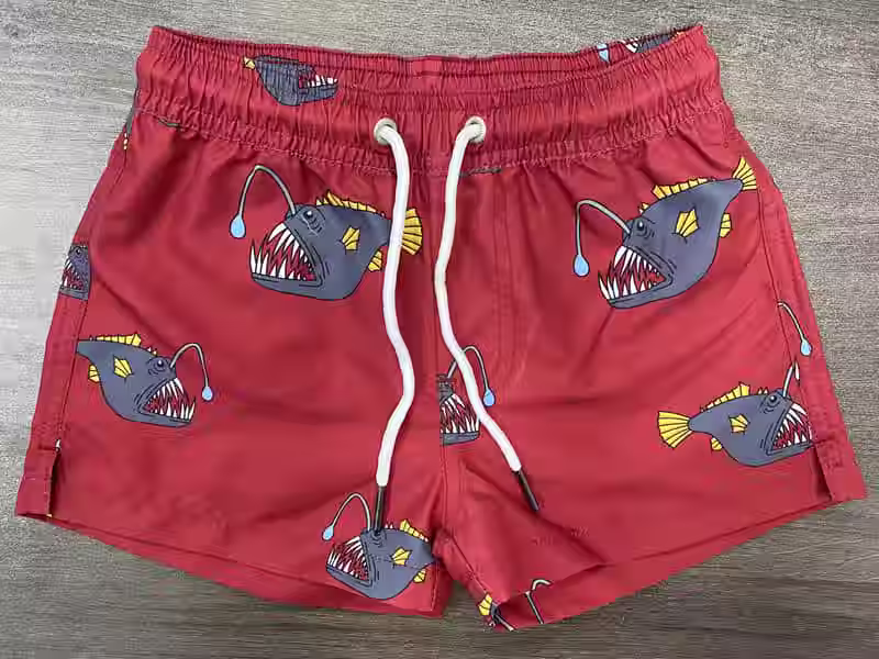 Front view of red elastic-waist swim shorts with large fish print