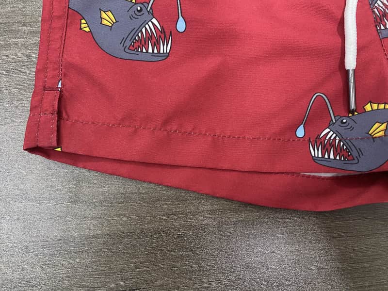 Hem and large fish motif detail on red swim shorts
